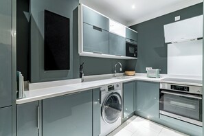 A modern kitchen with grey cabinets, a built-in washing machine, a microwave, and a double oven. - Bohemian Living in the Heart of Marylebone - Pass the Keys (London)