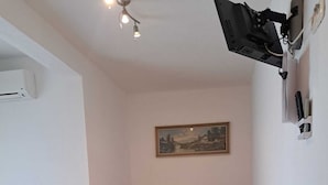 Een woonkamer met een bank, een bijzettafeltje en een aan de muur bevestigde televisie.