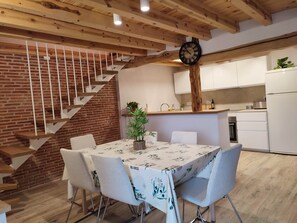 A dining area with a table set for four, a staircase with wooden railings, and a kitchen with white cabinets and a clock on the wall.