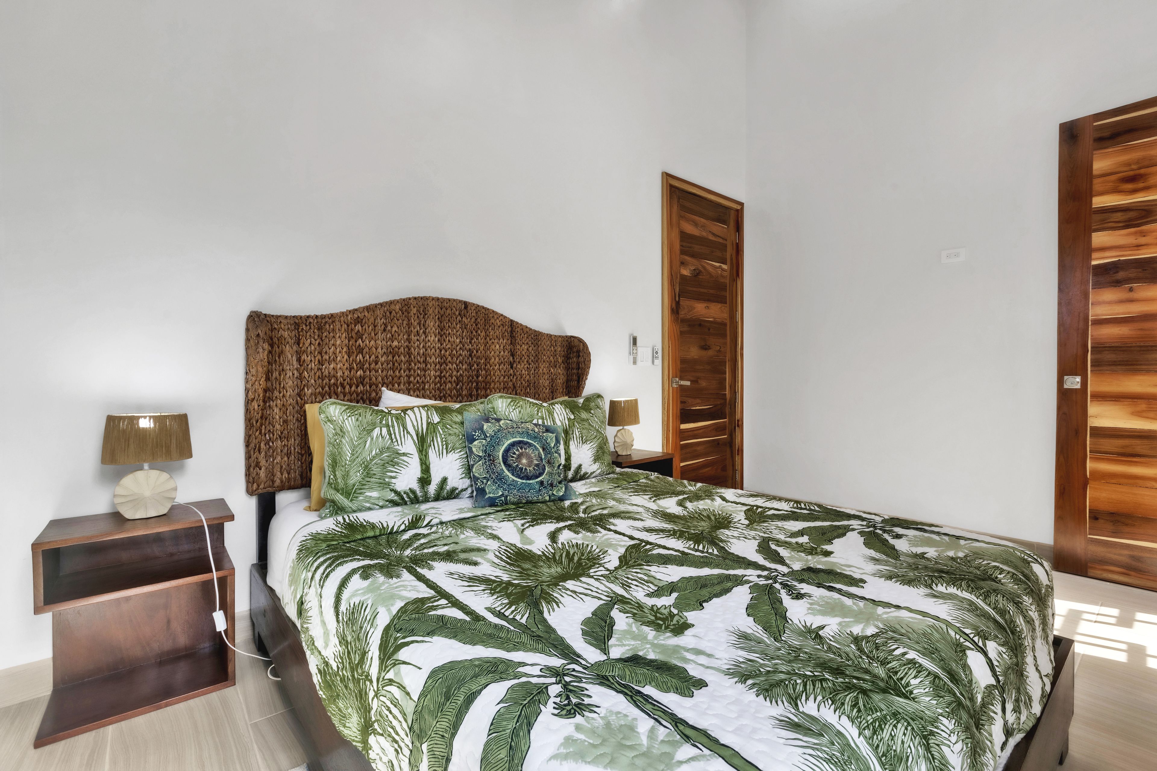 Une chambre à coucher comprenant un lit, des tables de chevet, une armoire en bois et un thermostat fixé au mur.