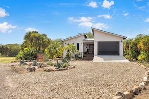 A modern house with a garage, surrounded by a gravel driveway and tropical plants.
