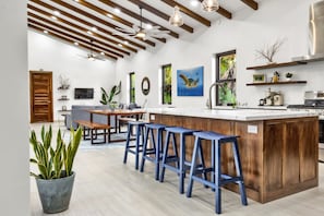 A modern kitchen with a wooden island, bar stools, a dining table, and a large window with a view of palm trees.
