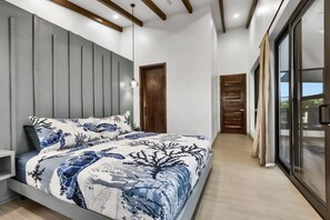 A modern bedroom with a large bed, a wooden door, and a view through a glass door.