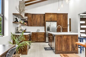 A modern kitchen with wooden cabinets, a stainless steel refrigerator, and a large island with a sink. - NAIA Residences - Brand New Luxury 3-Bedroom Villa with Private Pool (Placencia)