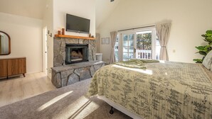 Ein Schlafzimmer mit Kamin aus Stein, einem Bett mit floralem Überwurf, einem Deckenventilator und Blick ins Freie durch ein Fenster.