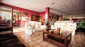 Un vestíbulo amplio con sofás estampados con motivos florales, una mesa de centro de madera y un mostrador de recepción.