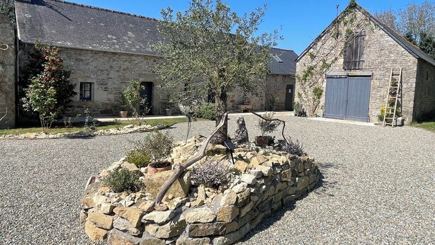 Ein Steinhaus mit Kiesweg und einem kleinen Gartenbereich mit Baum und Topfpflanzen.