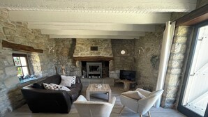 Ein gemütliches Wohnzimmer mit Steinwänden, einem Kamin, einer Couch und zwei Sesseln.