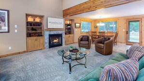 A cozy living room with a fireplace, a glass coffee table, a green sofa, and a dining area with wooden furniture. - THRU09-Contemporary Sunriver Getaway with AC, Hot Tub (Sunriver)