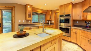A kitchen with wooden cabinets, stainless steel appliances, and a central island with a sink. - THRU09-Contemporary Sunriver Getaway with AC, Hot Tub (Sunriver)