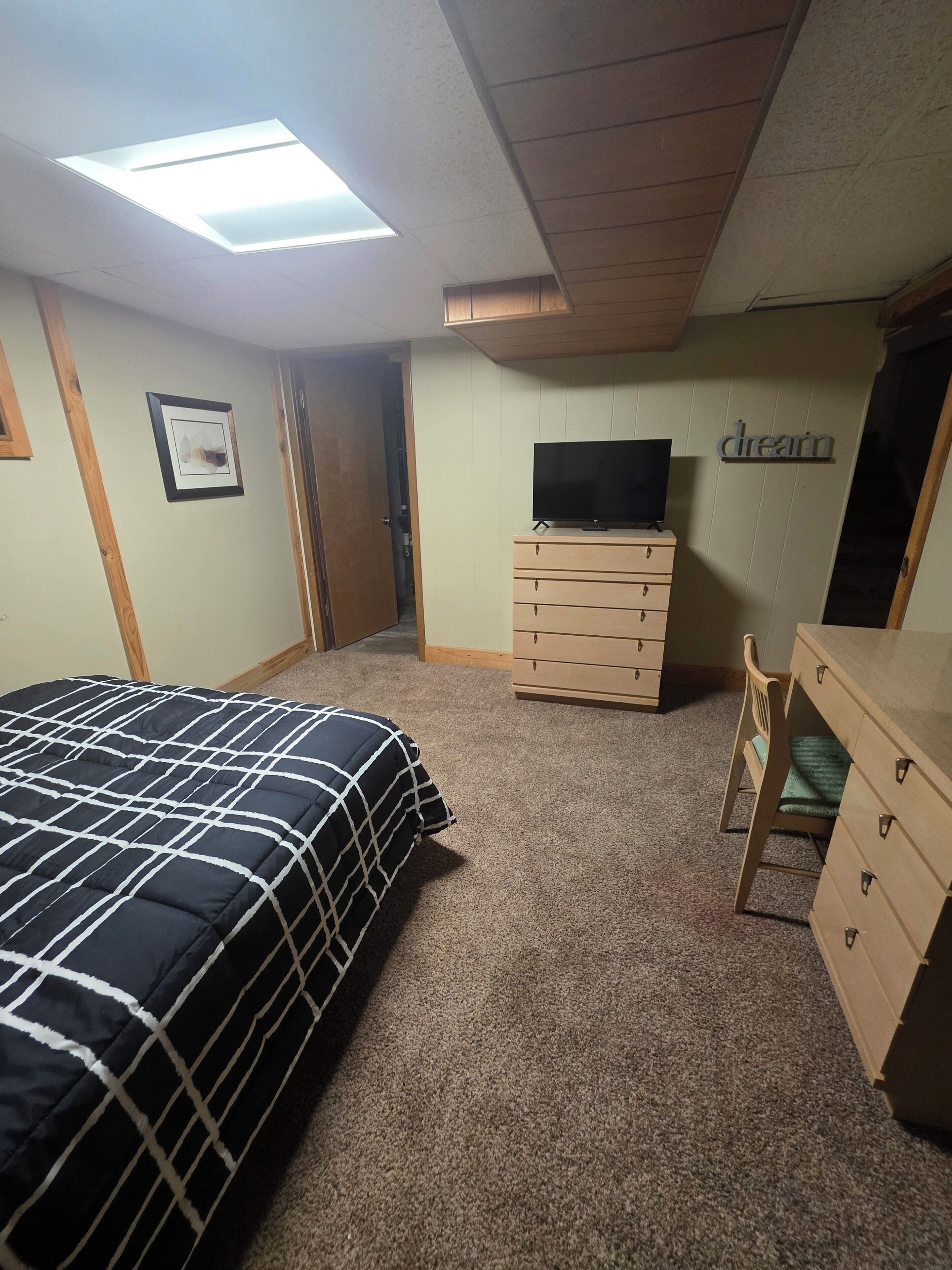 Een slaapkamer met een bed, een dressoir, een televisie en een plafondlamp.