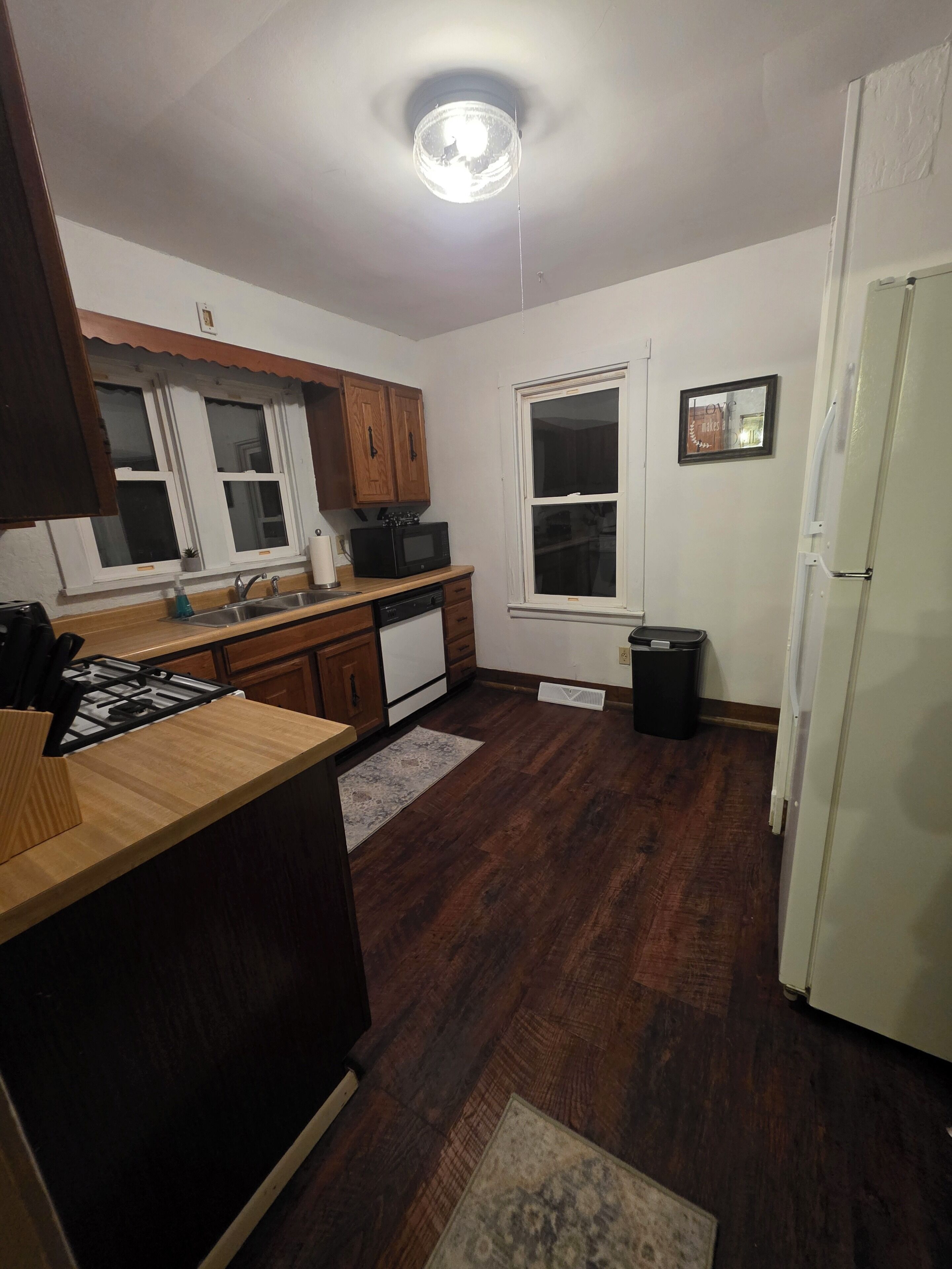 A kitchen with wooden cabinets, a microwave, a stove, a sink, and a refrigerator.