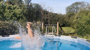 A swimming pool with clear blue water, surrounded by greenery and a wooden deck. - CLOS DU PIN - 6 pers ( Gite N°2 du domaine du Pin) (LANGUIDIC)