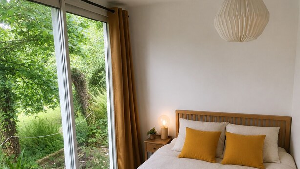 A bedroom with a large window, a bed with two pillows, a bedside table with a lamp, and a hanging light fixture. - CLOS DU PIN - 6 pers ( Gite N°2 du domaine du Pin) (LANGUIDIC)