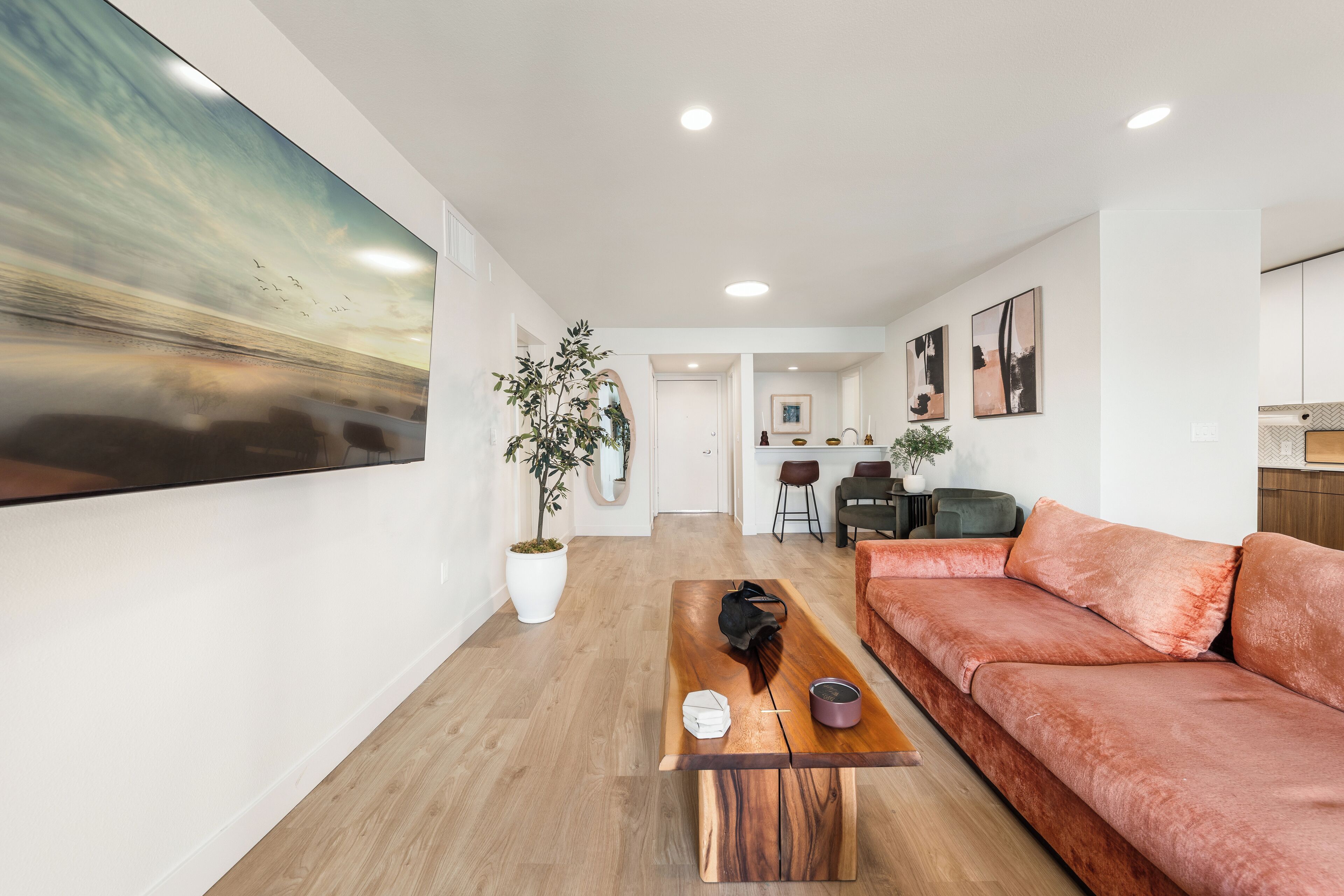 A modern living room with a large painting, a wooden coffee table, a sofa, and a potted plant.