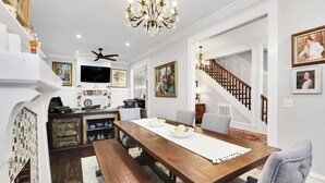 A dining area with a wooden table, white walls, and a chandelier. There is a staircase with wooden railings leading to another level.