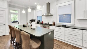 A modern kitchen with white cabinetry, a central island with bar stools, a stainless steel range hood, and pendant lighting.