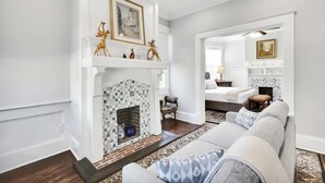 A living room with a fireplace, a sofa, a chair, and a bed in the background.