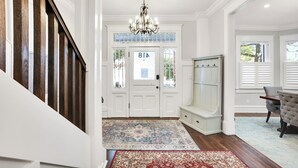 A hallway with a wooden staircase, a chandelier, a patterned rug, and a bench.