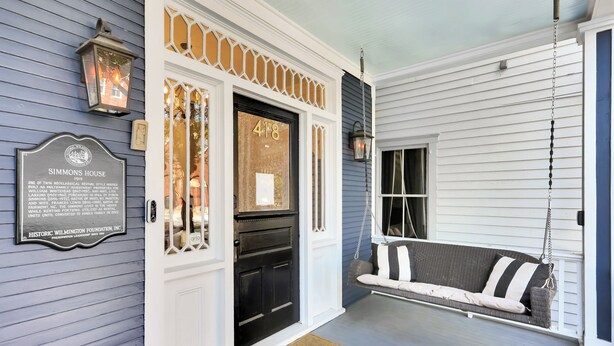 A porch with a swing seat, a black door with the number 418, and a welcome mat.