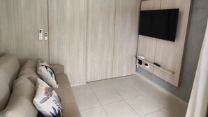 A modern living room with a beige sofa, a ceiling fan, a mounted TV, and a wall-mounted air conditioner. - Carneiros Beach Resort (Tamandaré)