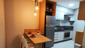 A compact kitchen with a wooden dining table, white chairs, a built-in oven, and a refrigerator. - Carneiros Beach Resort (Tamandaré)