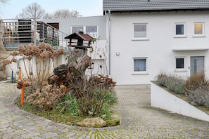 Ein Wohngebäude mit Treppe, einem kleinen Garten mit vertrockneten Pflanzen und einem Kiesweg.