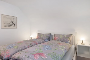 Ein Doppelbett mit floraler Bettwäsche, zwei Nachttische mit Lampen und ein gerahmtes Bild an der Wand.
