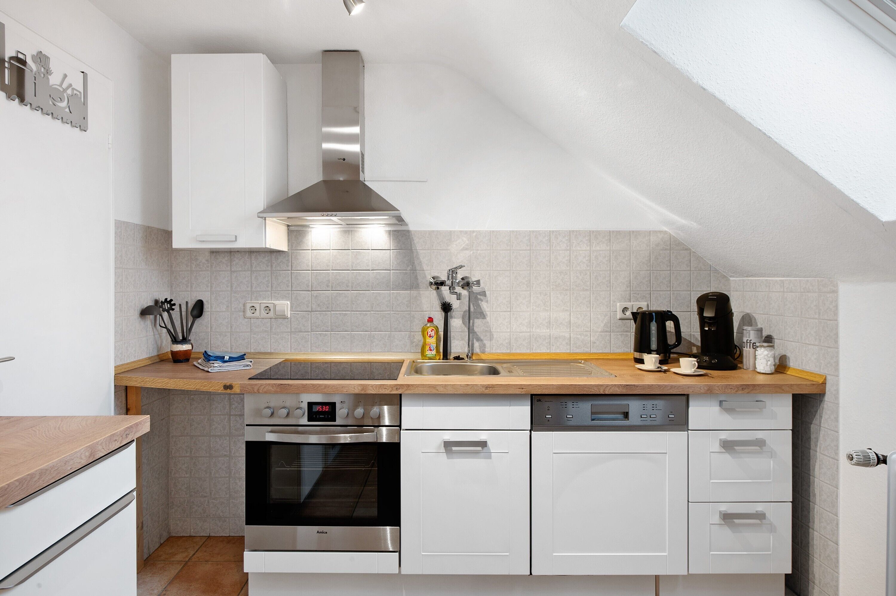 Una cocina moderna con armarios blancos, electrodomésticos de acero inoxidable, encimera de madera y salpicadero de azulejos.