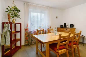 Een eetgedeelte met een houten tafel en stoelen, een hangplant en een raam met bloemen gordijnen.