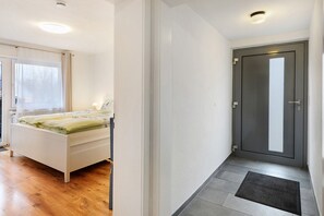 A bedroom with a bed, a window with curtains, a door, and a hallway with a mat. - Apartment 'Kastanie' with Mountain View, Shared Garden and Wi-Fi (Müllheim)