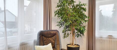 A room with a leather chair, a potted plant, and a view of a house through a window.