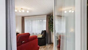 A room with a red sofa, a black armchair, a glass door, and a plant. - Apartment 'Kastanie' with Mountain View, Shared Garden and Wi-Fi (Müllheim)