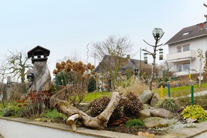 A garden with a bird feeder, a wooden structure, and a house in the background. - Apartment 'Kastanie' with Mountain View, Shared Garden and Wi-Fi (Müllheim)
