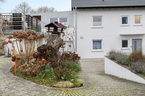 Een woongebouw met een trap, een kleine tuin met verdorde planten en een pad van stenen.