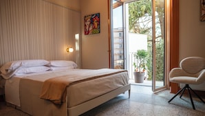 A bedroom with a bed, a chair, a painting, and a view of the outside. - Charming Historic Home with Garden Views in the Heart of Acireale (Acireale)
