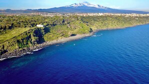 An aerial view of a coastal area with a mountain in the background, terraced fields, and a small white building near the shore. - Charming Historic Home with Garden Views in the Heart of Acireale (Acireale)