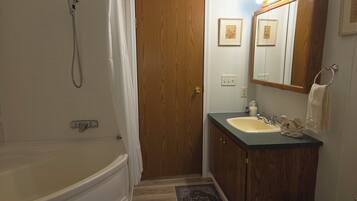 A bathroom with a bathtub, a wooden door, a sink with a mirror, and a towel rack.