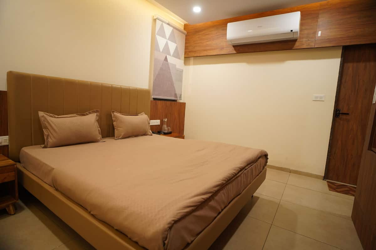 Un dormitorio con una cama grande, cabecera de madera, mesita de noche, aire acondicionado de pared y una puerta.