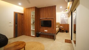 A modern living room with a flat-screen TV mounted on a wooden wall, a wooden bench, a small table, and a ceiling fan. - RAAHI HOMESTAY (Ujjain)