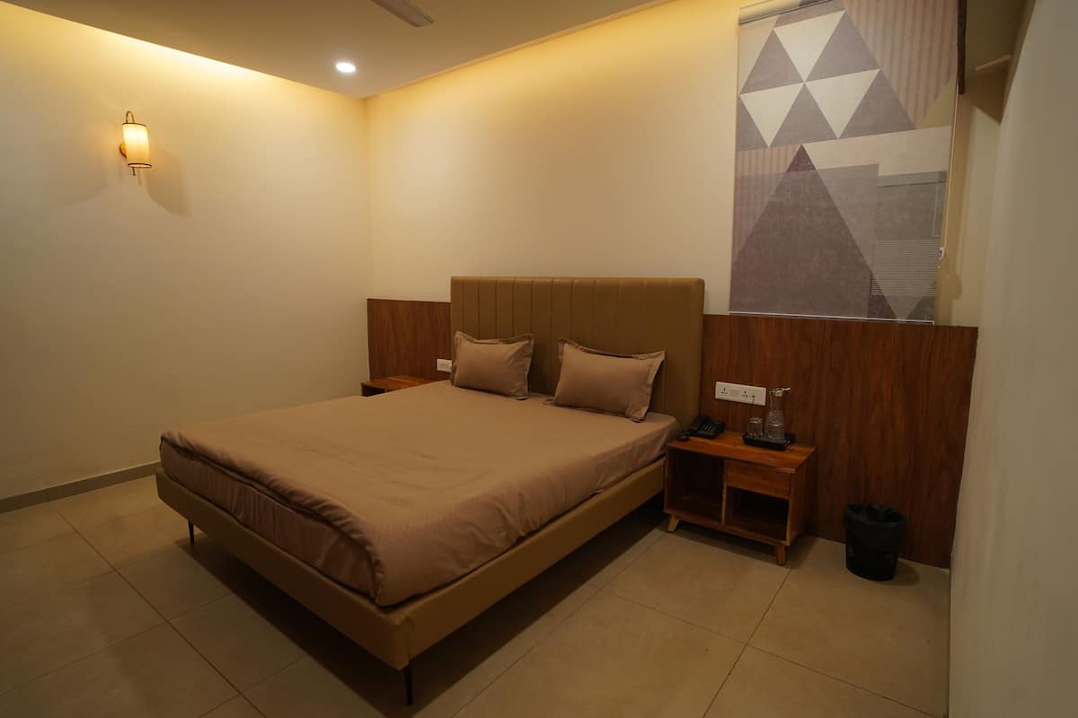 Una habitación de hotel moderna con una cama grande, cabecera de madera, mesitas de noche y una lámpara fijada a la pared.