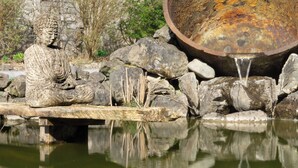 A Buddha statue in a garden with a pond and a large metal basin. - CastleHacket House (Tuam)