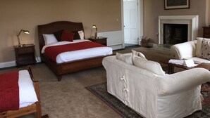 A bedroom with a large bed, a sofa, a fireplace, and a door leading to another room. - CastleHacket House (Tuam)