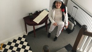 A person standing in a hallway with a checkered floor, a framed picture on the wall, a table with a document, and a suitcase on the floor. - CastleHacket House (Tuam)