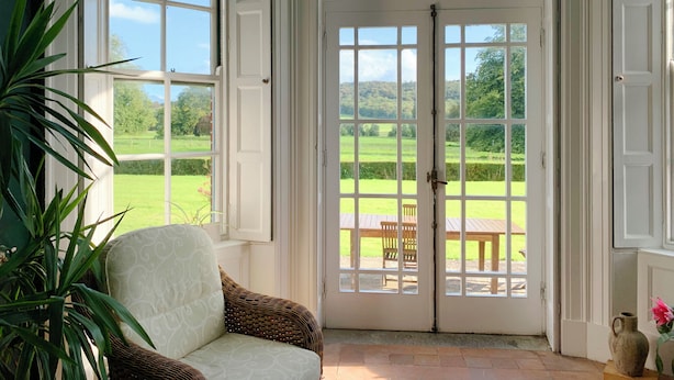 A conservatory with a large arched door, a wicker chair, and a view of a green landscape. - CastleHacket House (Tuam)