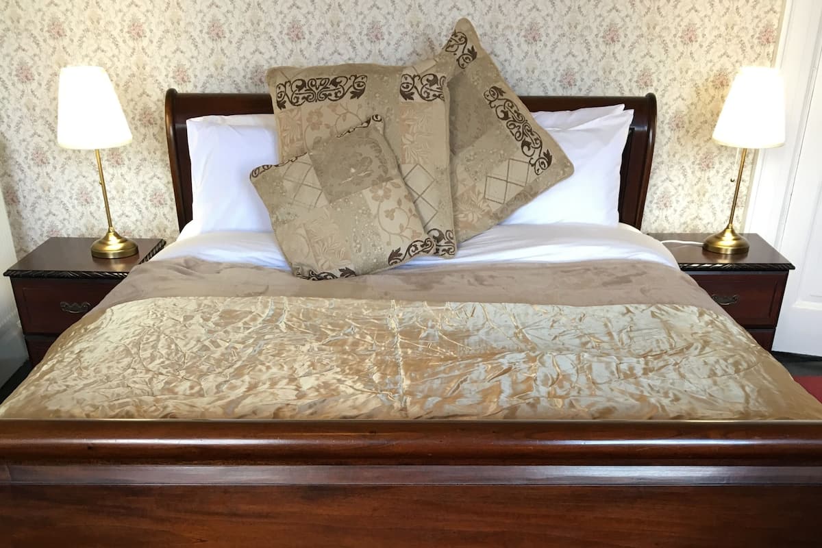 A neatly made bed with a patterned bedspread and two decorative pillows, flanked by nightstands with lamps.