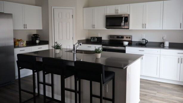 A modern kitchen with white cabinets, a central island with bar stools, a microwave, oven, and coffee maker. - Clean and Cozy home with AC (Haines City)