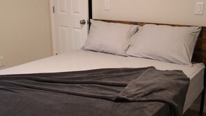 A bedroom with a bed, white bedding, a dark grey blanket, and a wooden headboard. - Clean and Cozy home with AC (Haines City)