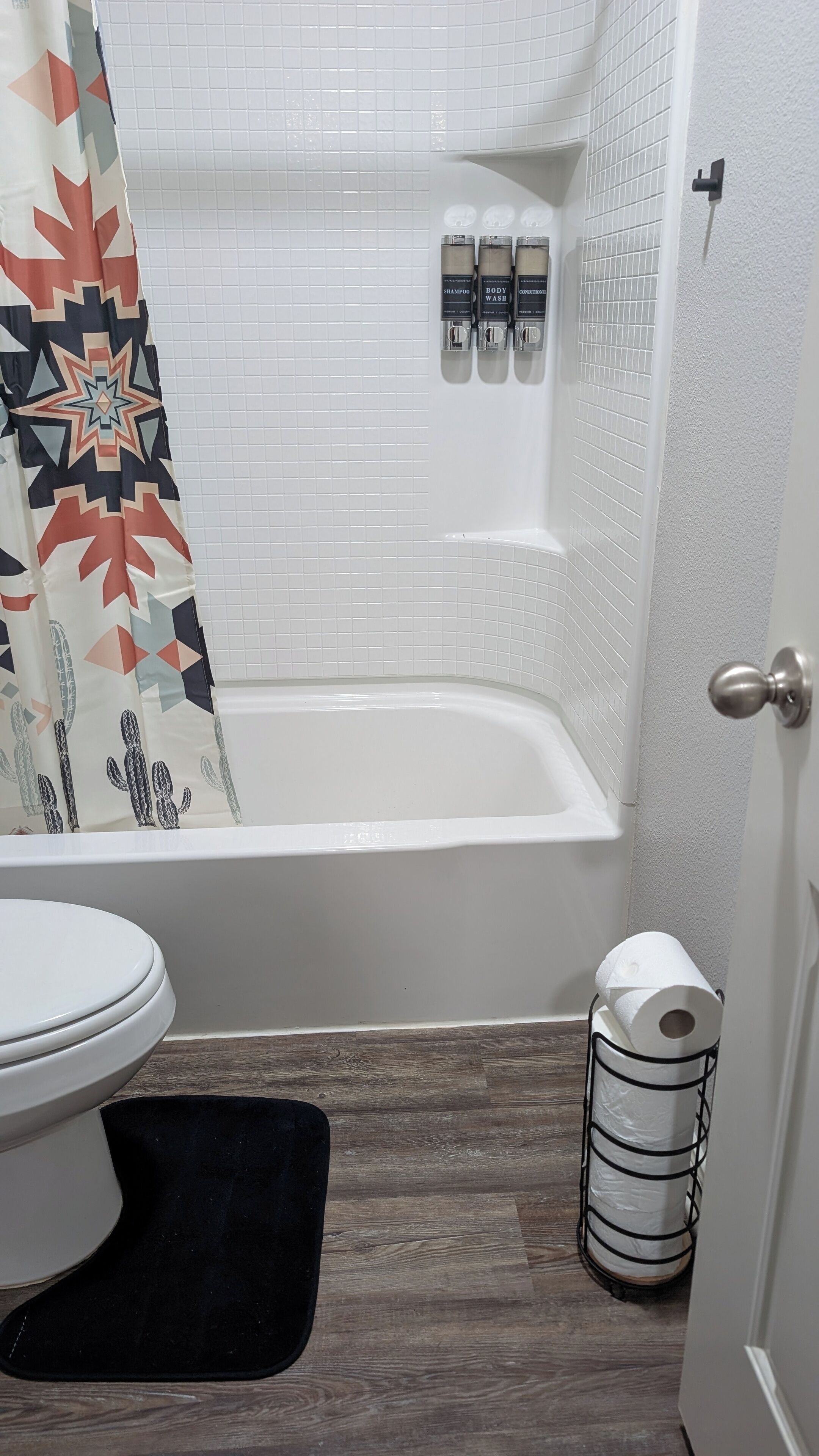 Et badeværelse med et hvidt badekar, toilet og et bruseforhæng med geometrisk mønster.