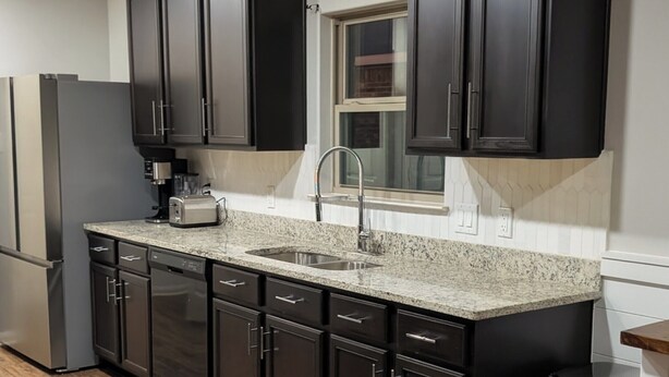 A modern kitchen with dark cabinetry, a granite countertop, and stainless steel appliances.